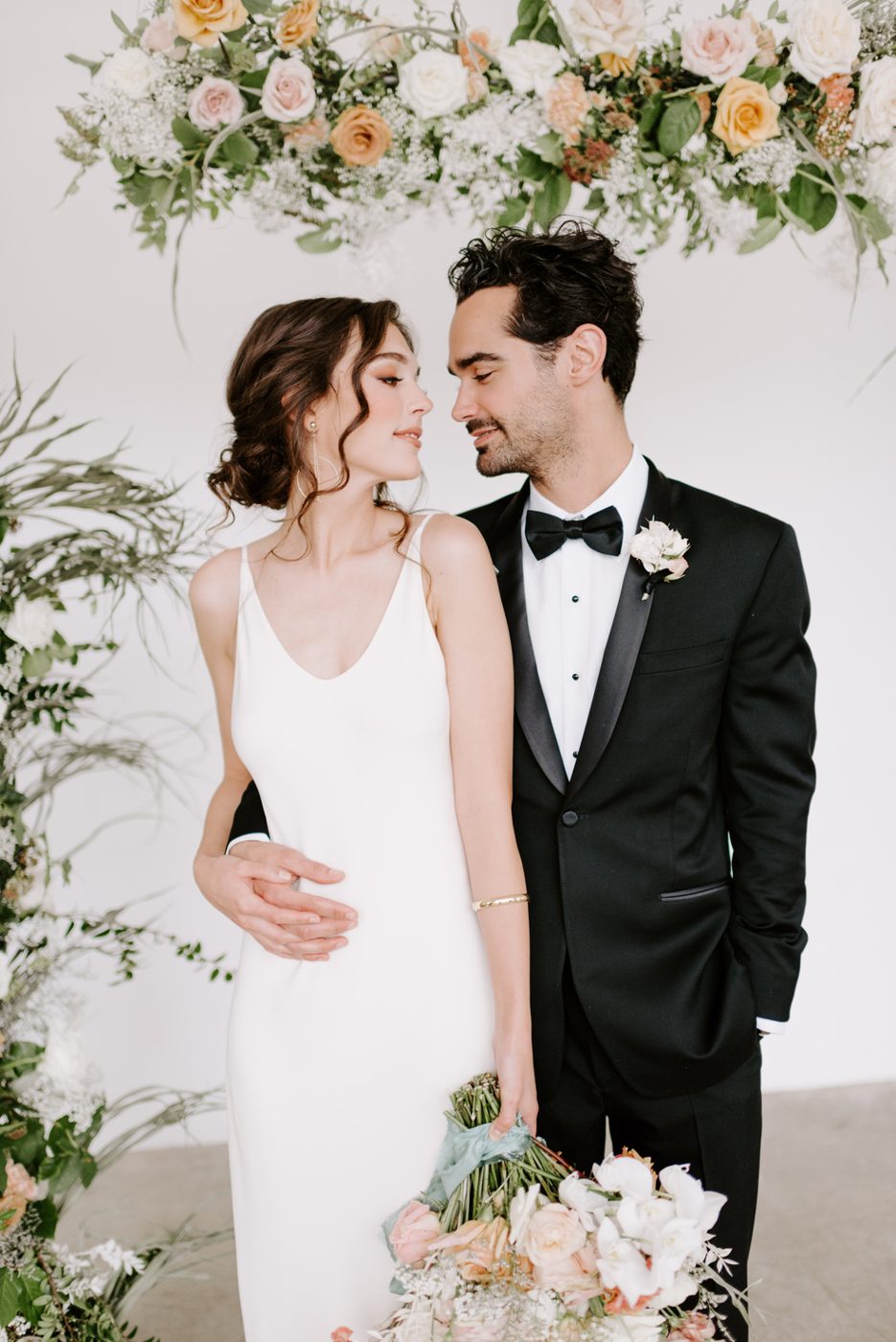 Couple beneath a floral arch, bride in a white slip dress