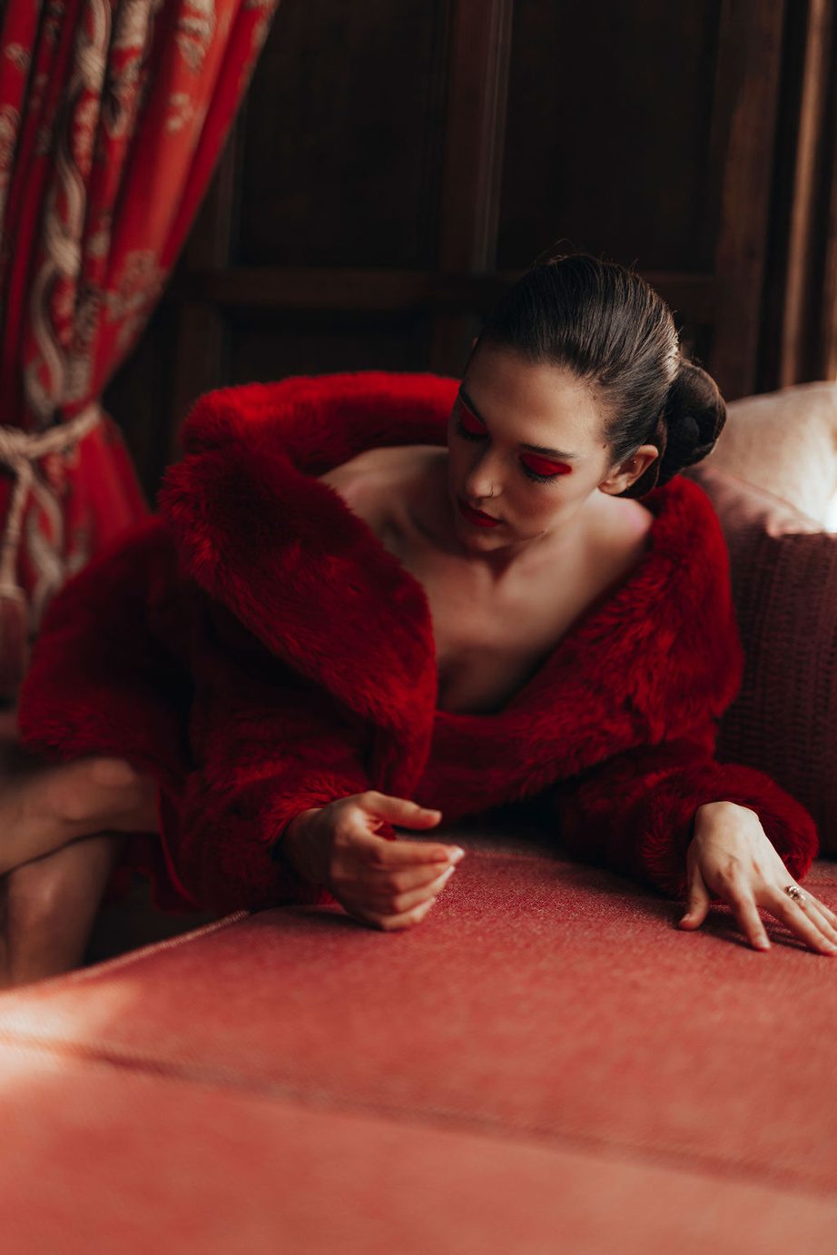 Reclining in a red fur coat against red upholstery