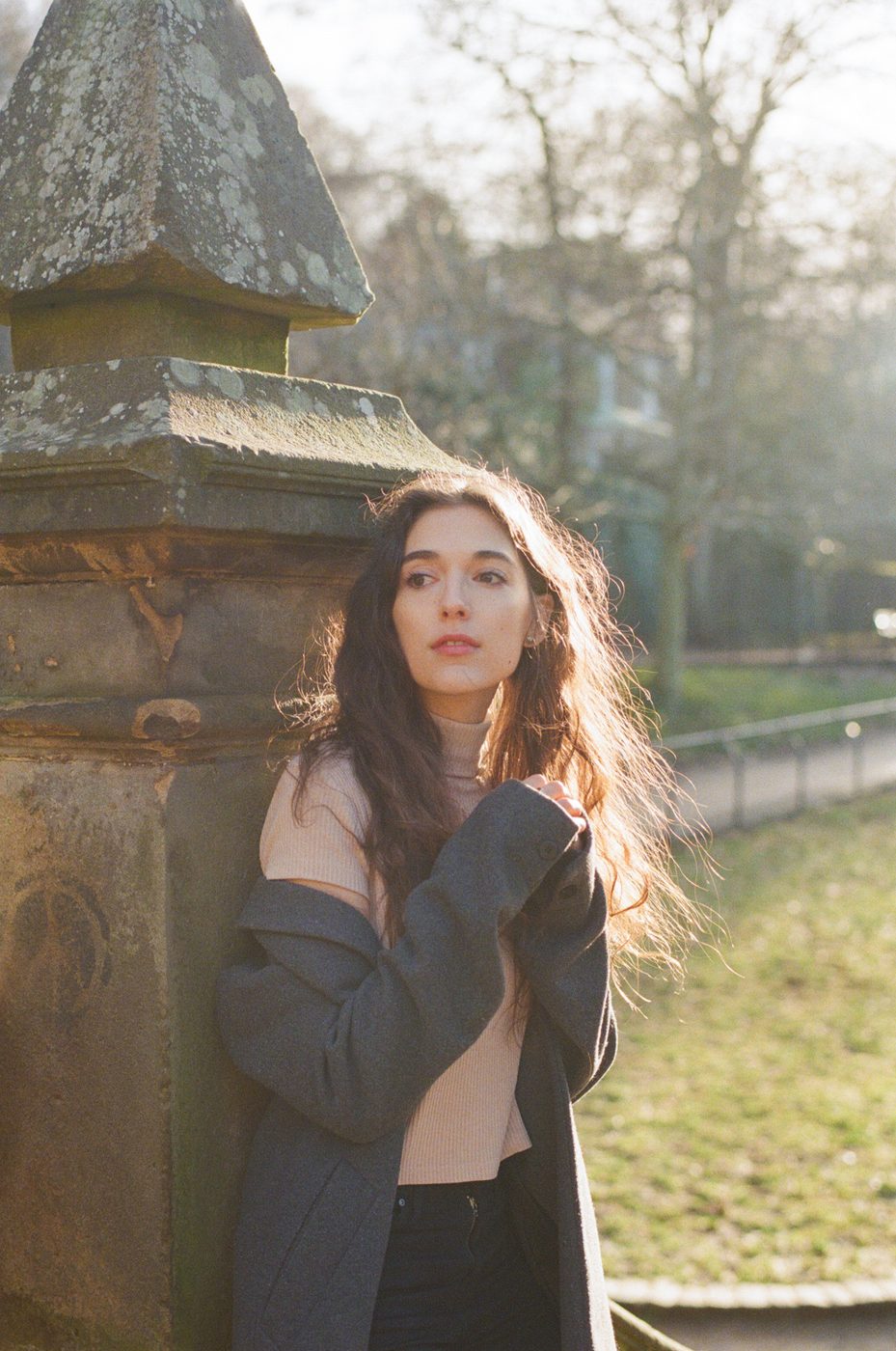 Leaning against a stone pillar in soft backlight