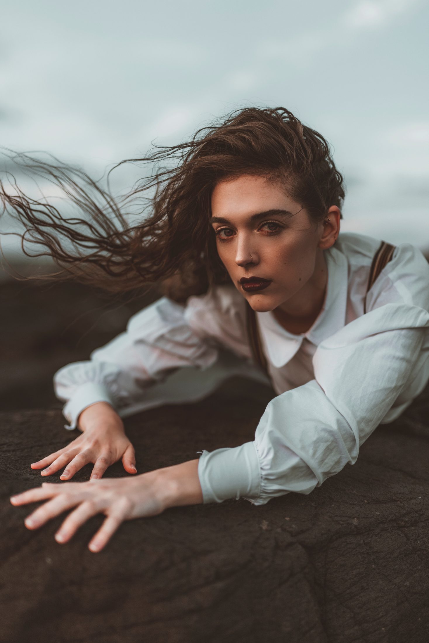 Caroline Nikolaus in a white shirt on dark rocks, hair caught by the wind